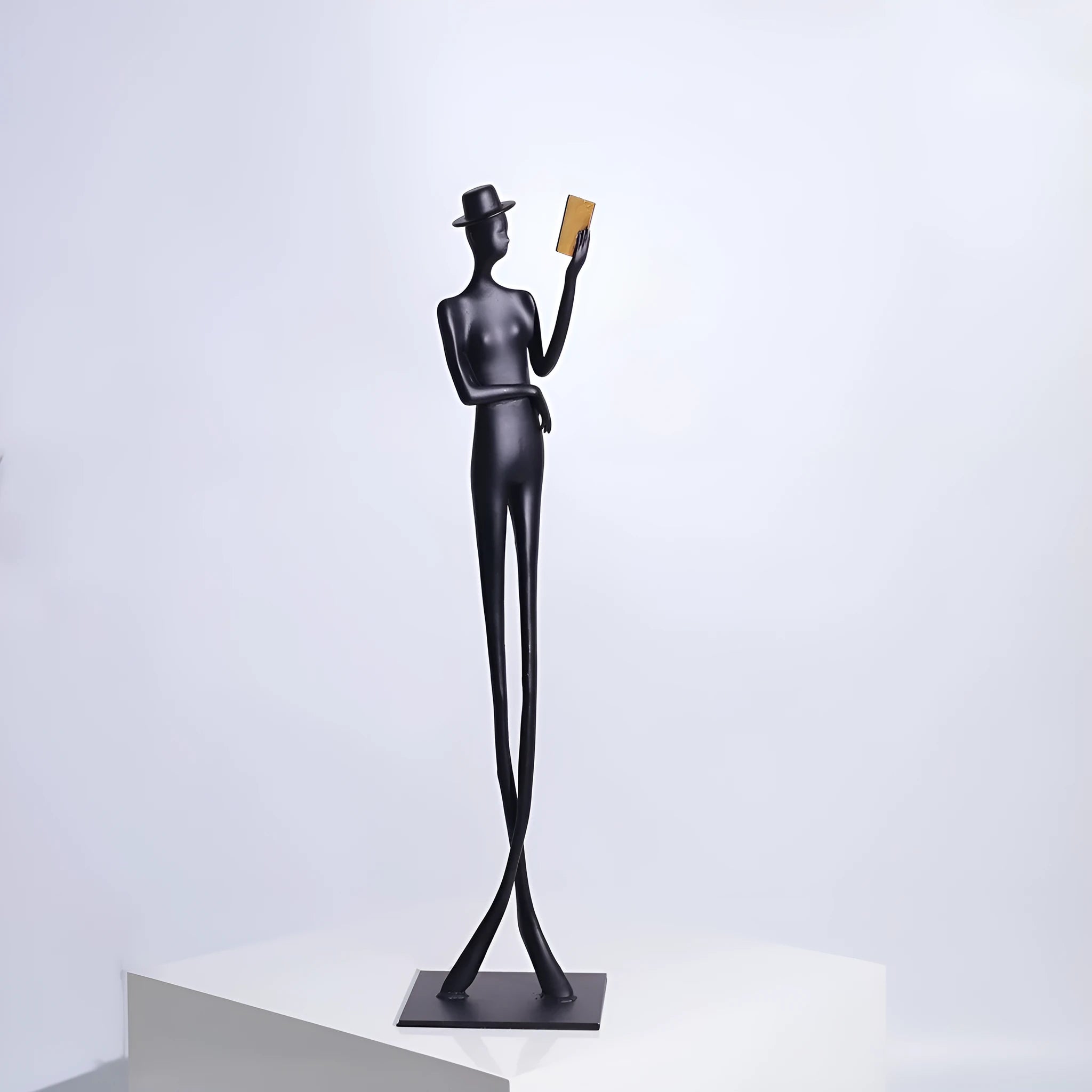 Black minimalist cast aluminum sculpture of a woman reading, 51cm tall on a desktop.