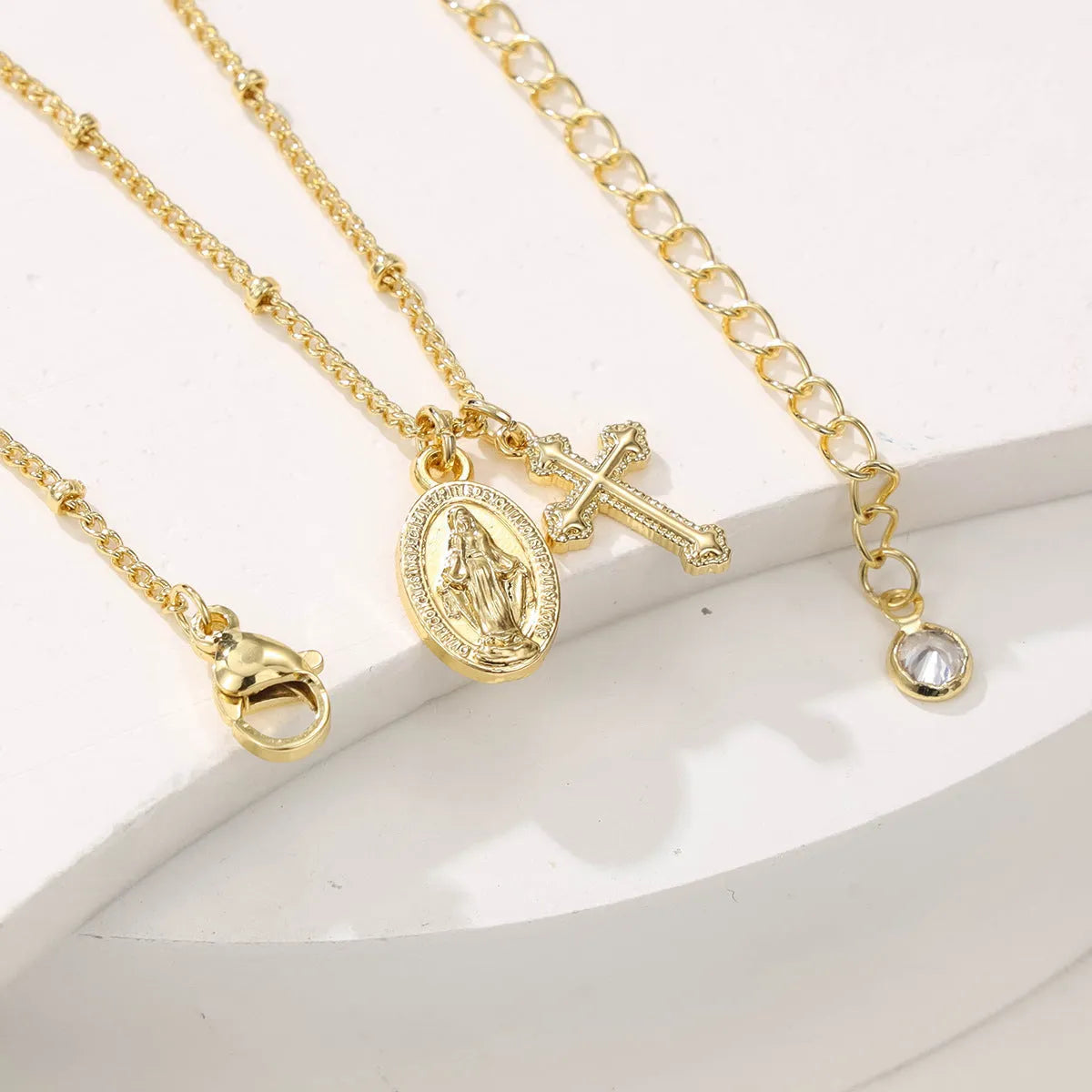 Gold geometric cross pendant necklace with Virgin Mary centre on a model.