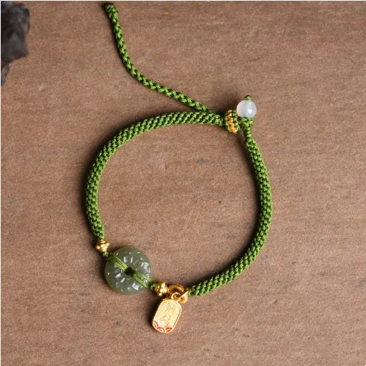 Close-up of a women's hand-woven green rope bracelet with a Hetian jade peace buckle charm.