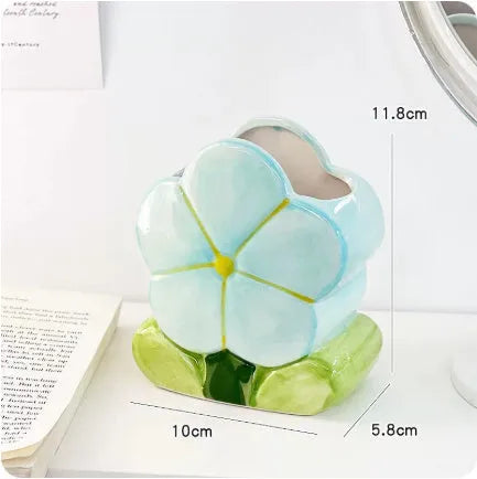 Ceramic pen holder box with floral decoration on a desk, holding pens.