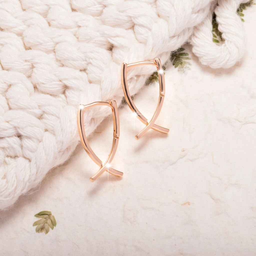 Rose gold coloured cross shaped earrings made from copper metal on a white background.