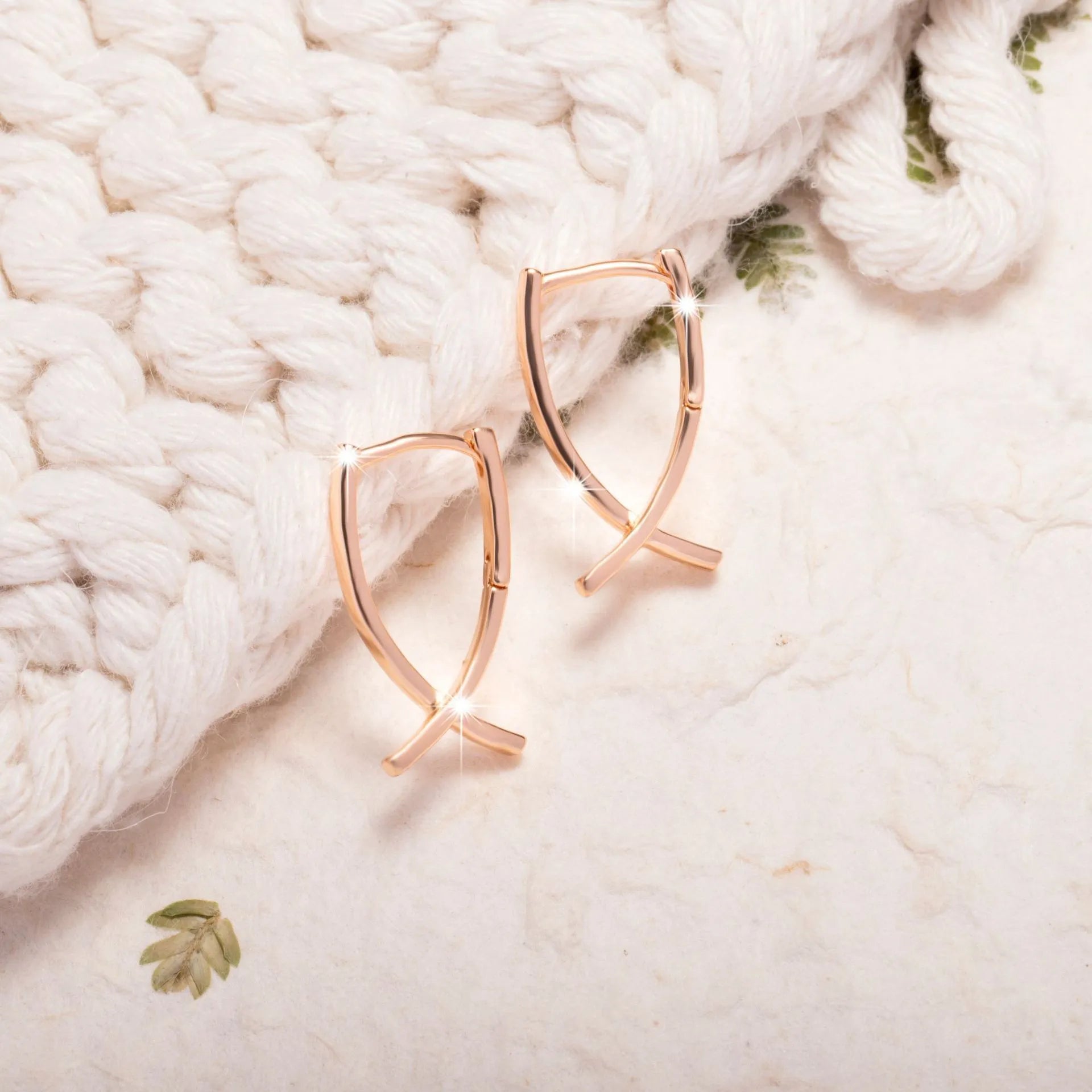 Rose gold coloured cross shaped earrings made from copper metal on a white background.