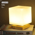 White Nordic solid wood USB table lamp with touch dimming in cube shape on a wooden table.