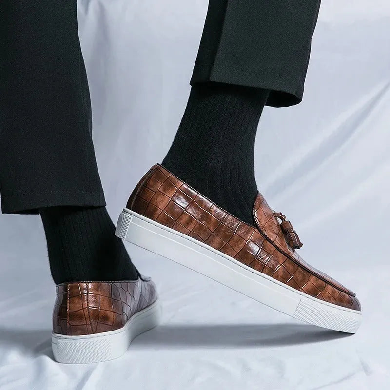Men's black smart-casual sneakers with a tassel detail on the front, showing a round toe and slip-on style.