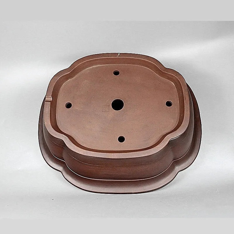 Handmade antique crabapple shaped purple clay flowerpot on a wooden floor.