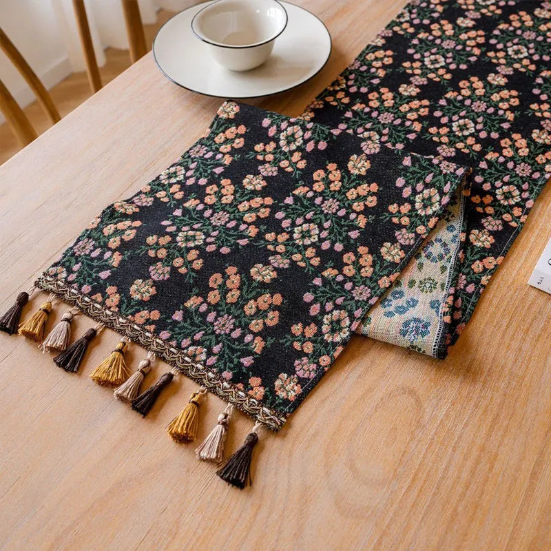Dark blue jacquard table runner with bouquet pattern and tassels laid on a wooden dining table.