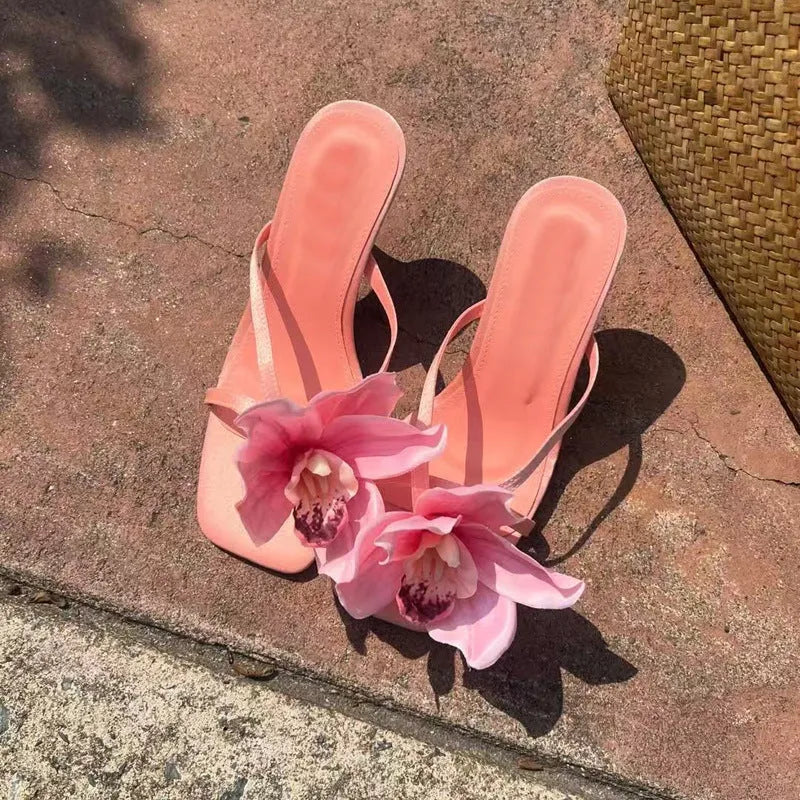 Pink women's sandals with artificial Phalaenopsis flower, satin upper, and mid heel.