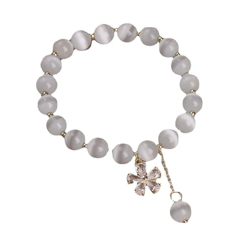 Close-up of a women's single loop bracelet with a white cat's eye stone, flower tassel, and pink morganite safety buckle pendant.