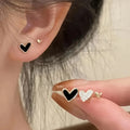 Three pairs of heart-shaped alloy earrings in gold, black, black and white, and pink colours on display.
