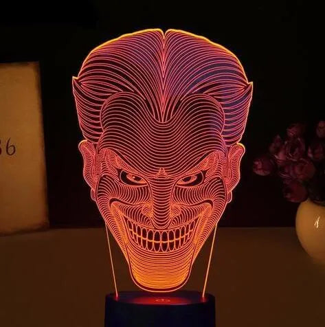 A 3D LED table lamp displaying multiple colours, with a remote control and USB cable on a desk.