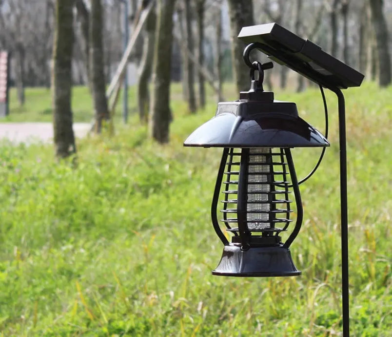 White outdoor solar mosquito lamp with solar panel on top and LED light beads, shown in a garden setting.