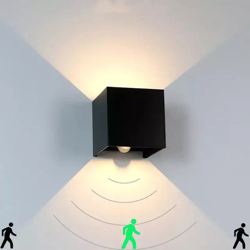 Square black aluminium wall lamp with 360-degree light output mounted on a corridor wall.
