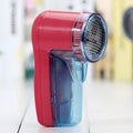 Portable electric lint remover shaver for clothing on a blue background.
