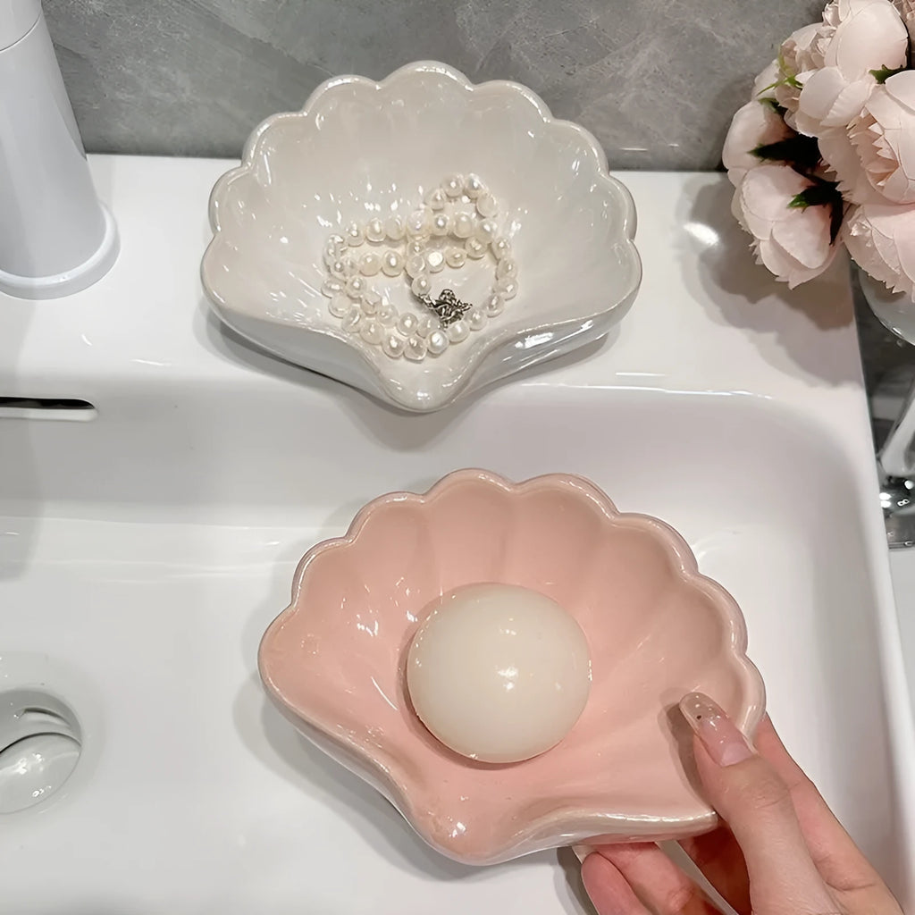 A white or pink plastic shell-shaped soap dish for bathroom counter or shower use.