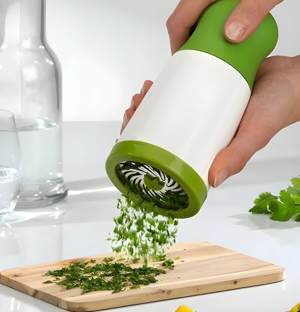 White and grey manual herb grinder with stainless steel blades and removable top on a kitchen counter.