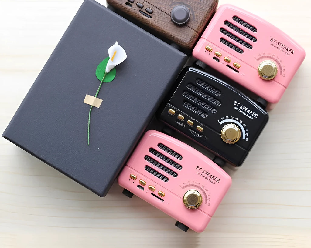 Compact vintage wood finish Bluetooth speaker in black, pink, or wood grain colour on a wooden surface.
