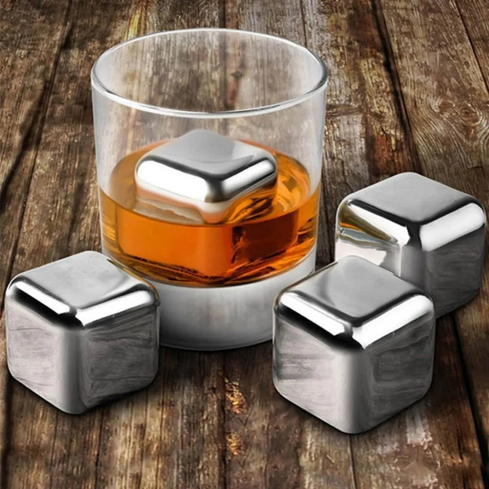 Set of stainless steel reusable whiskey stones in various shapes with metal tongs on a wooden surface.
