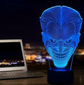 A 3D LED table lamp displaying multiple colours, with a remote control and USB cable on a desk.