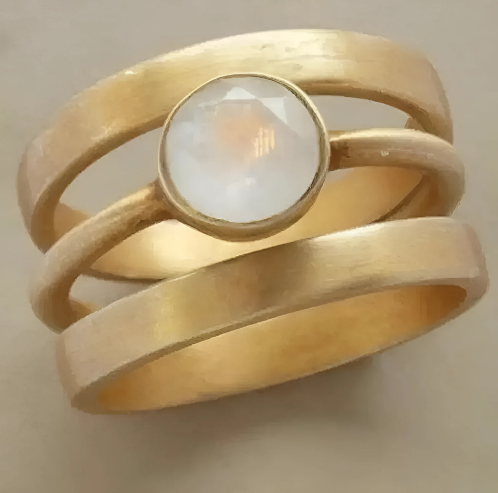 A gold geometric ring with a hollow design and a small inlaid white chalcedony stone on a titanium steel band.