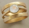 A gold geometric ring with a hollow design and a small inlaid white chalcedony stone on a titanium steel band.