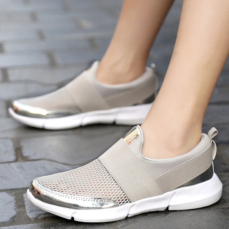 A pair of blue, low-cut women's casual sneakers with a mesh lining on a hard floor surface.
