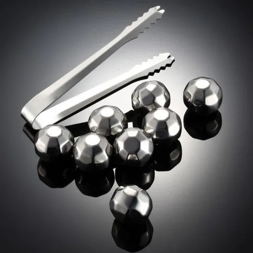 Set of stainless steel reusable whiskey stones in various shapes with metal tongs on a wooden surface.