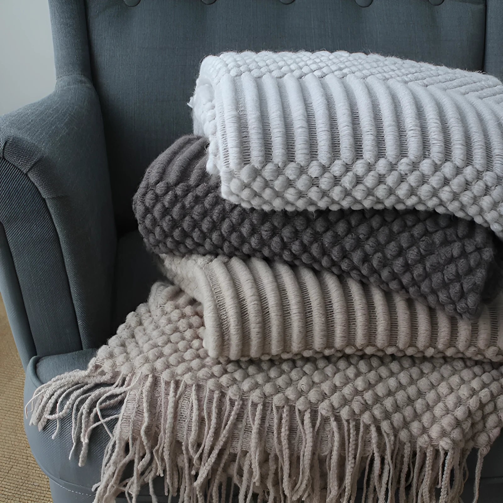 Small grey polyester nap blanket folded on a sofa, showing its size and texture.