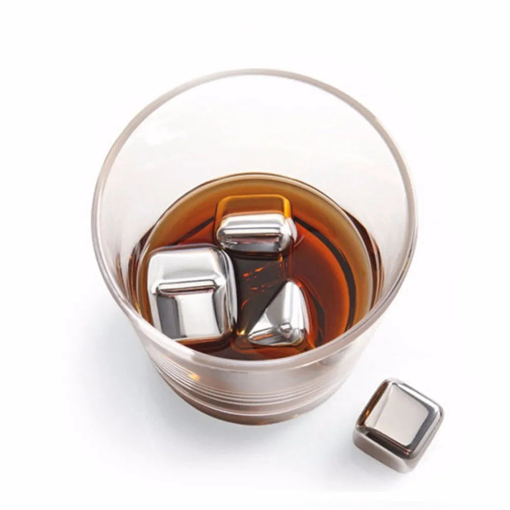 Set of stainless steel reusable whiskey stones in various shapes with metal tongs on a wooden surface.