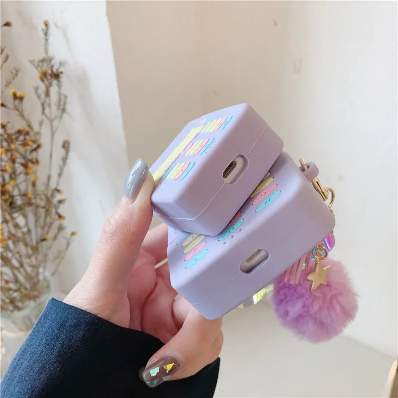 Purple silicone clamshell case for Apple AirPods with a small white fur ball pendant attached.