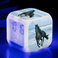 Square cartoon-style alarm clock with digital LED display showing time, placed on a wooden surface.