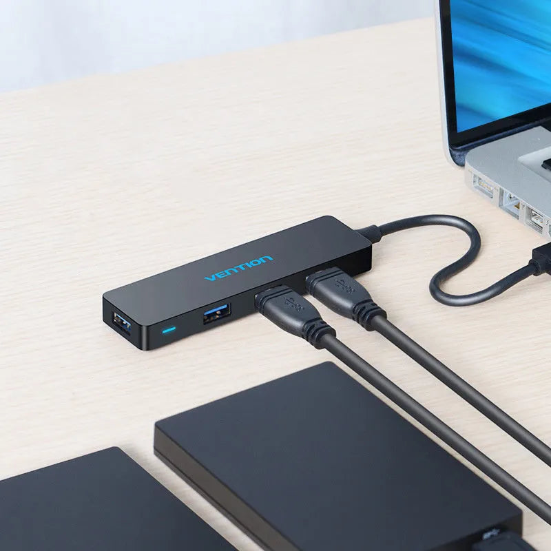 Black four-port USB 3.0 hub with a short cable on a desk.