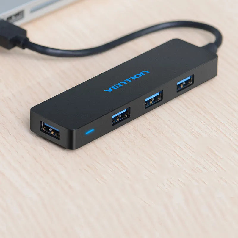 Black four-port USB 3.0 hub with a short cable on a desk.