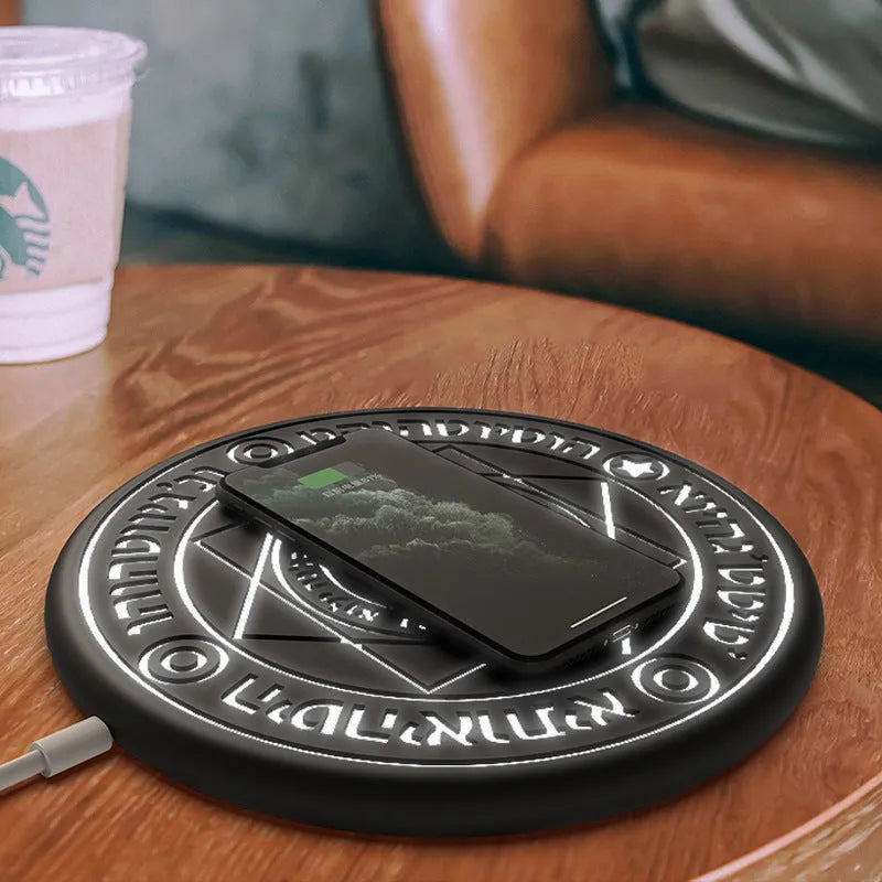 Square black wireless charging pad with glowing magic array pattern, charging a mobile phone.