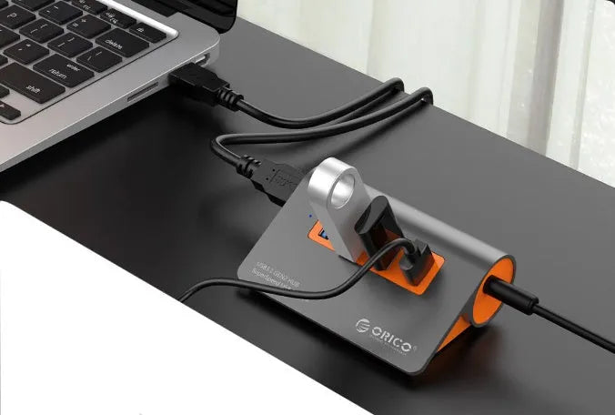 Dark grey and orange aluminium USB-C hub with four USB ports, a blue LED light, and a separate data cable.