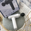 Black, red, and grey handheld fascia massage gun on a table with USB cable.