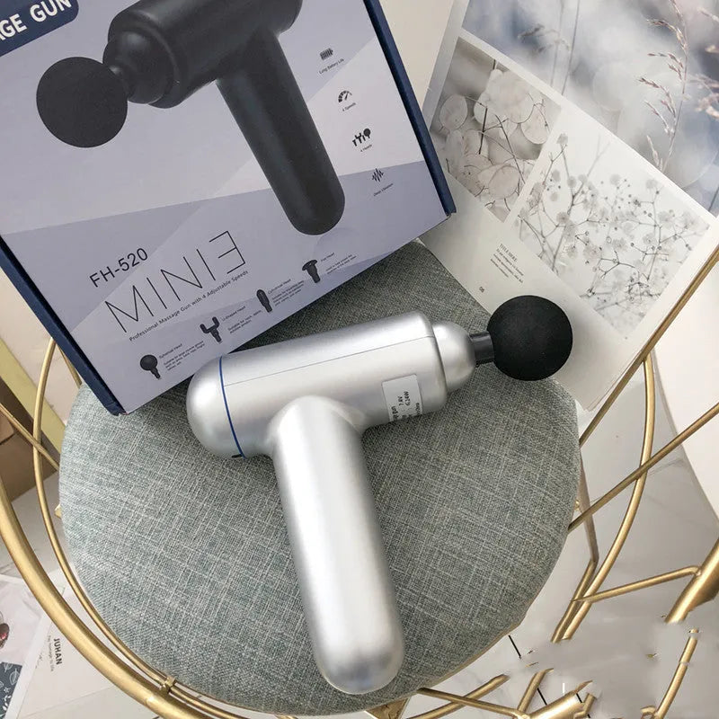 Black, red, and grey handheld fascia massage gun on a table with USB cable.