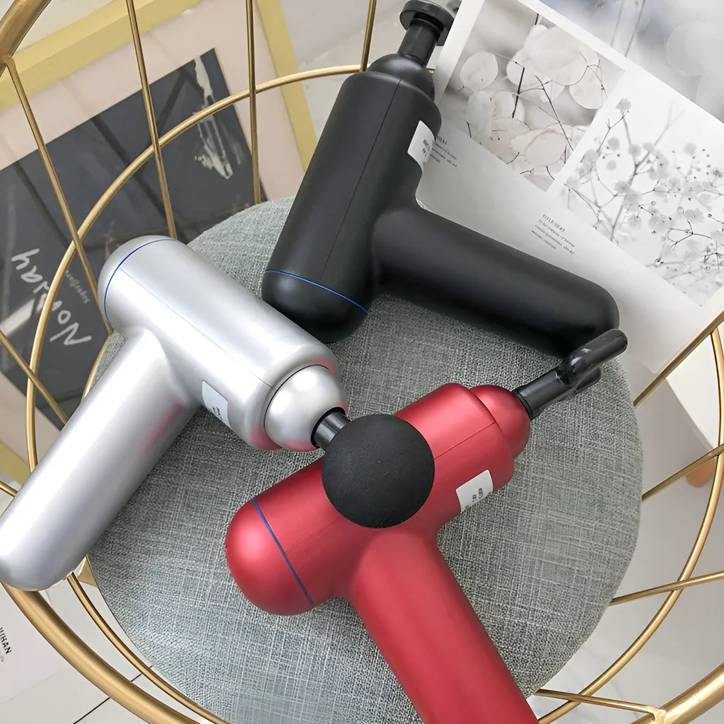 Black, red, and grey handheld fascia massage gun on a table with USB cable.