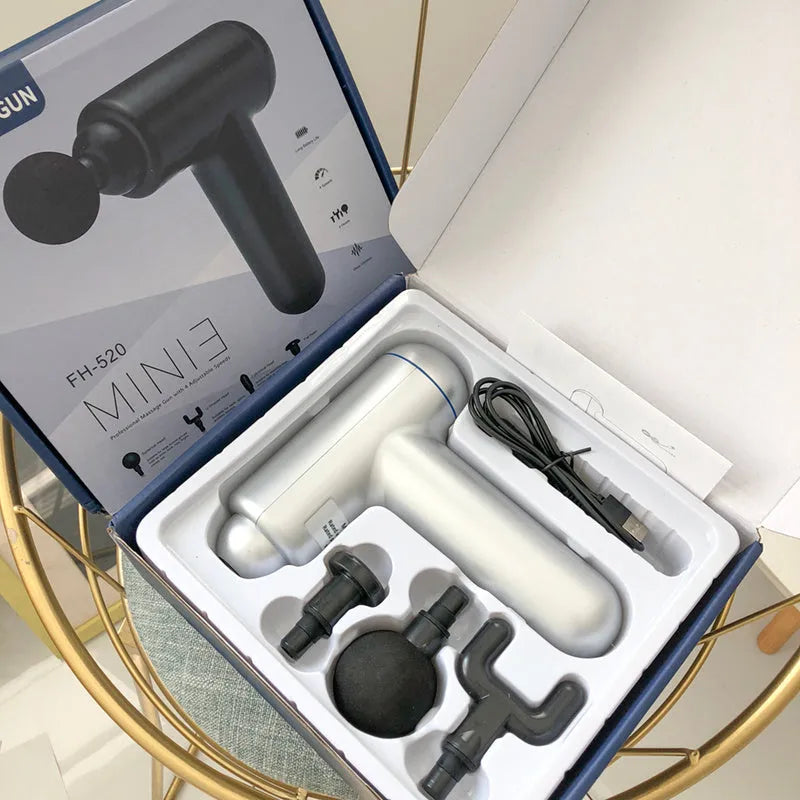 Black, red, and grey handheld fascia massage gun on a table with USB cable.