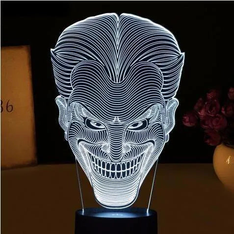 A 3D LED table lamp displaying multiple colours, with a remote control and USB cable on a desk.