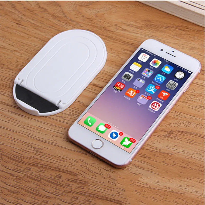 Plastic lazy bracket mobile phone stand in six colour options holding a smartphone on a wooden desk.