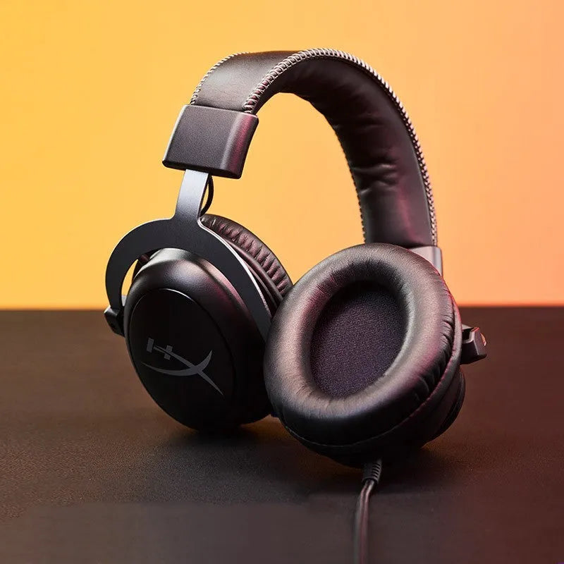 Black and red wired gaming headset with detachable microphone and separate USB sound card remote control on a desk.