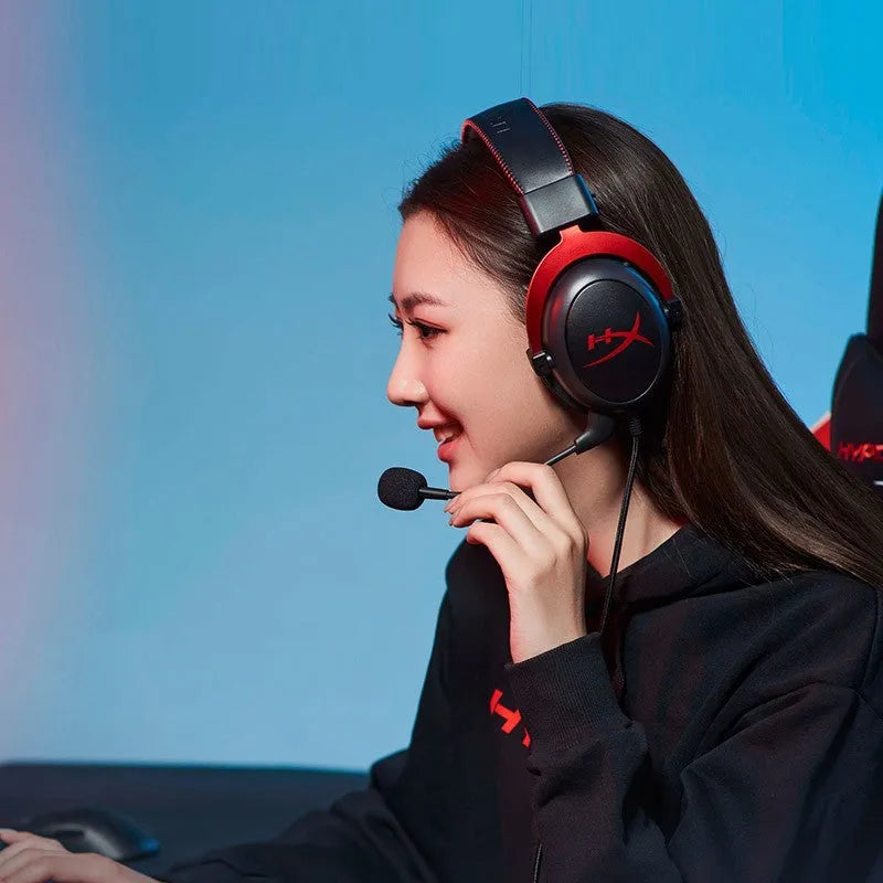 Black and red wired gaming headset with detachable microphone and separate USB sound card remote control on a desk.