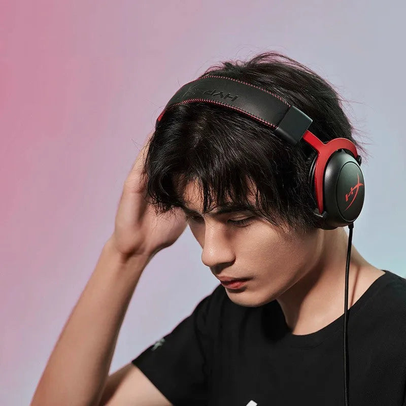 Black and red wired gaming headset with detachable microphone and separate USB sound card remote control on a desk.