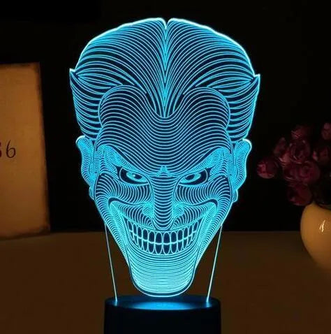 A 3D LED table lamp displaying multiple colours, with a remote control and USB cable on a desk.