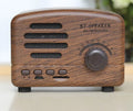 Compact vintage wood finish Bluetooth speaker in black, pink, or wood grain colour on a wooden surface.
