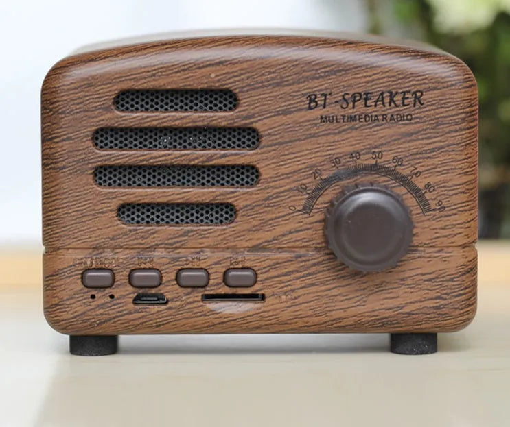 Compact vintage wood finish Bluetooth speaker in black, pink, or wood grain colour on a wooden surface.