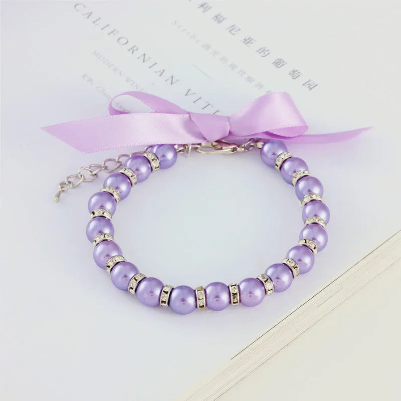 Small dog wearing adjustable pearl and rhinestone necklace with ribbon bow collar