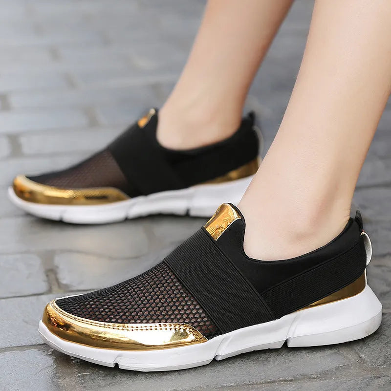 A pair of blue, low-cut women's casual sneakers with a mesh lining on a hard floor surface.
