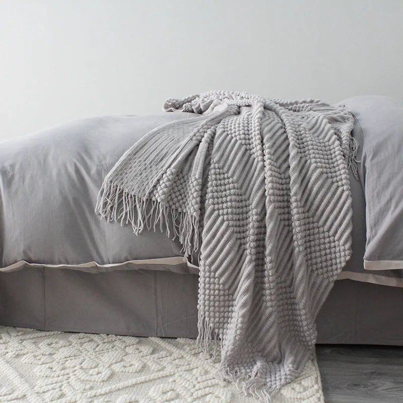 Small grey polyester nap blanket folded on a sofa, showing its size and texture.