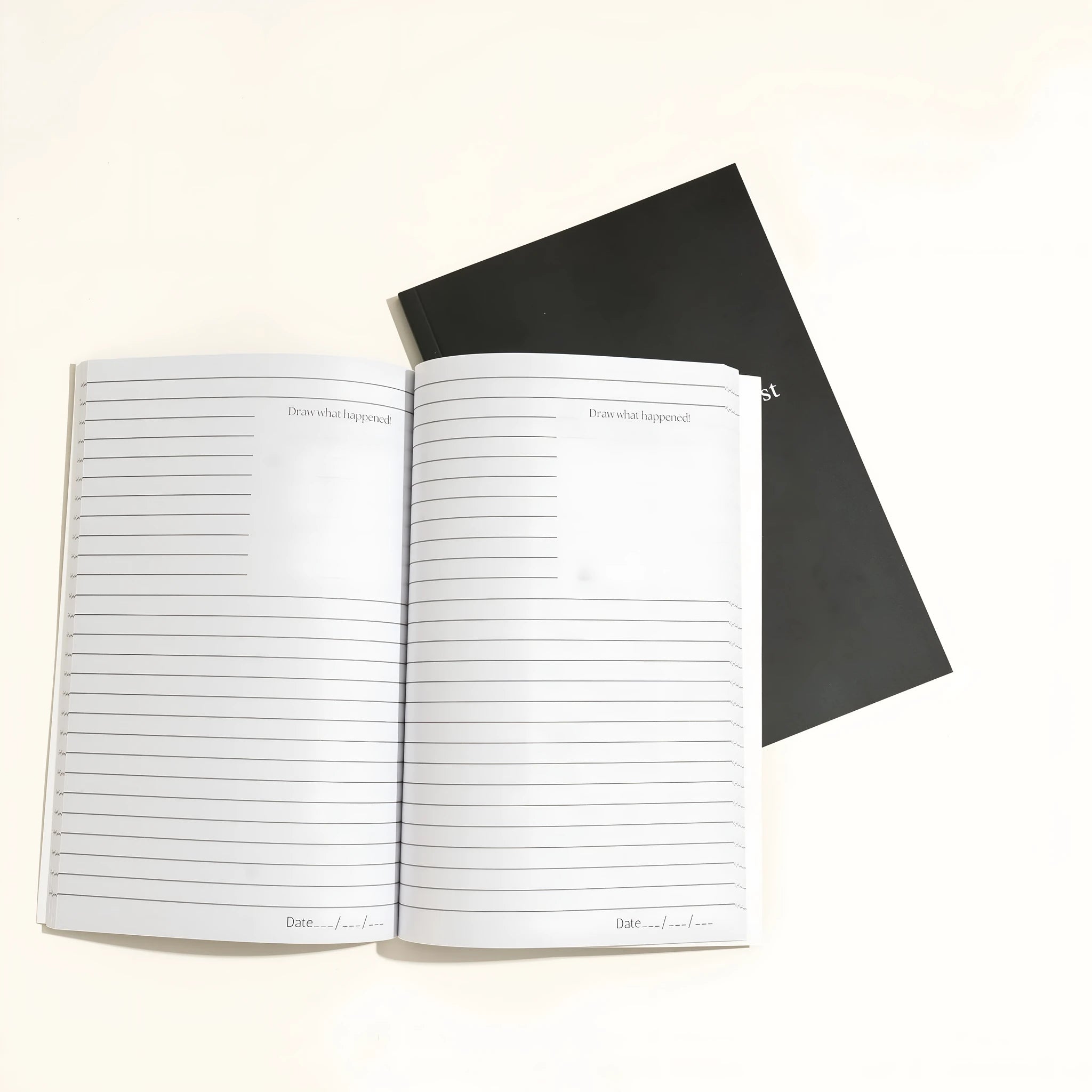Black hardcover A5 dream journal notebook with lined pages open on a surface.